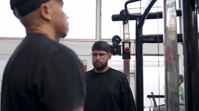 Personal trainer instructs a client performing bicep curls on a cable machine inside a gym