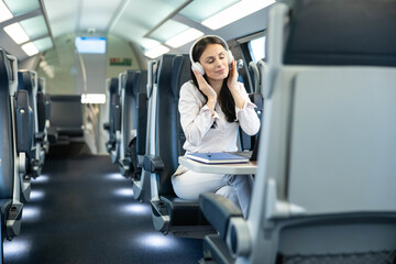 Obraz premium A serene woman, immersed in her music, sits in a modern train cabin, showcasing the blend of travel and personal enjoyment in a minimalist environment.