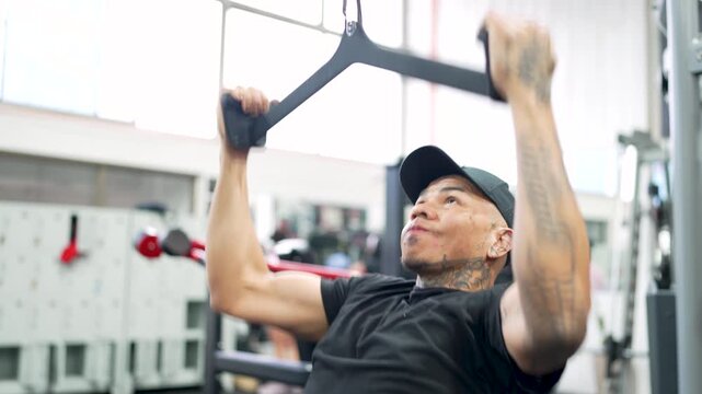 Young man with tattoos building back muscle with lat pulldown machine at the gym