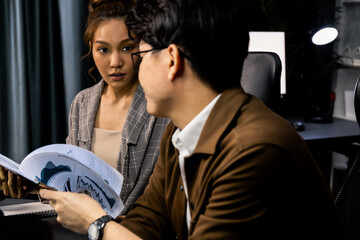 Serious face of working sales manager discussing on report data analysis paperwork with coworker at over late night at modern office, focusing on marketing plan project job social online. Infobahn.