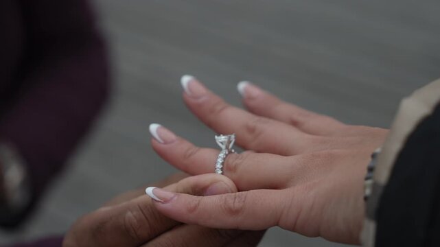 CloseUp Hands With Engagement Ring, Partner Sliding Diamond Band Onto Finger During Intimate Outdoor Proposal On Wooden Boardwalk,