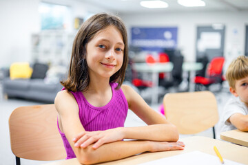 Smiling schoolgirl sitting at a desk in a modern STEM classroom, looking confident and engaged. Concept of future education, digital learning, creativity, and smart kids. Ideal for back-to-school