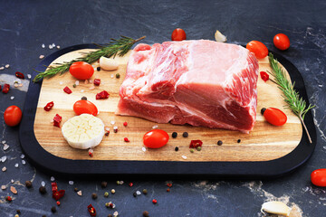 Raw pork neck or tenderloin on a wooden cutting board, garnished with cherry tomatoes, garlic and rosemary sprigs.