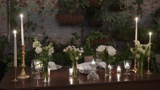 Formal Long Table Dinner In Loft, Event Planner Finalizing Seating, MaTre D Adjusting Candles, Caterer Inspecting Glassware Candlelit