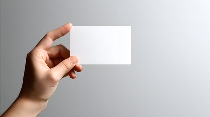 Obraz premium Person holding blank white rectangular card against subtle gray background with copy space