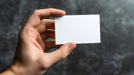 Person holding blank rectangular white card against dark textured background