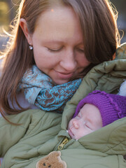 A girl with a child in a sunny winter forest. A mother holds her daughter in a park. The woman smiles at her newborn. The baby is wearing a winter jacket.
