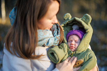 A girl with a child in a sunny winter forest. A mother holds her daughter in a park. The woman smiles at her newborn. The baby is wearing a winter jacket.