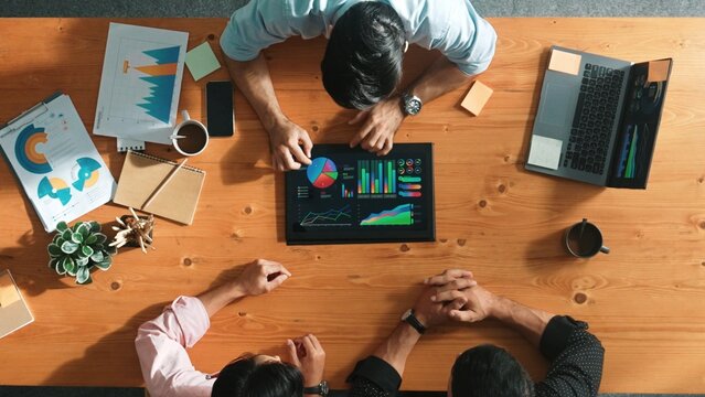 Top aerial view of business man present financial graph to group of smart investors. Professional male leader analyze graph and explain marketing idea by using tablet on meeting table. Convocation. - Powered by Adobe