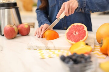 Woman cutting fruits for blending at white marble table indoors, closeup