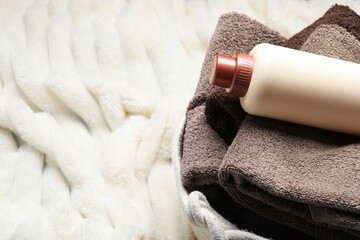 Laundry basket with towels and bottle of detergent on soft blanket, closeup. Space for text