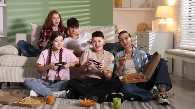 Group of teenagers playing video game and having snacks at home