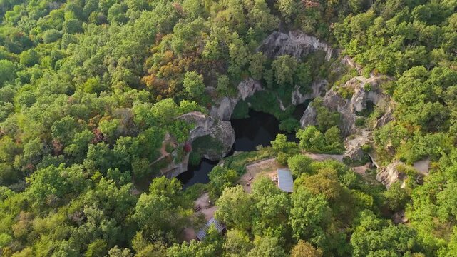 Orbiting aerial view of the Tarn of Megyer-hegy near S&aacute;rospatak, Hungary, showcasing lush greenery, rocky formations, and tranquil waters in a stunning millstone quarry turned nature preserve.