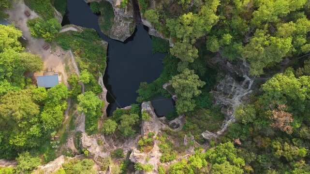 Tilt-down drone view of the Tarn of Megyer-hegy near S&aacute;rospatak, Hungary, revealing a beautiful lake surrounded by lush greenery and forest within a historic millstone quarry turned nature preserve.