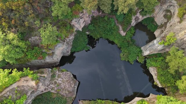 Tilt-down aerial view of the Tarn of Megyer-hegy near S&aacute;rospatak, Hungary, featuring a serene lake surrounded by lush greenery, rocky formations, and a historic millstone quarry.