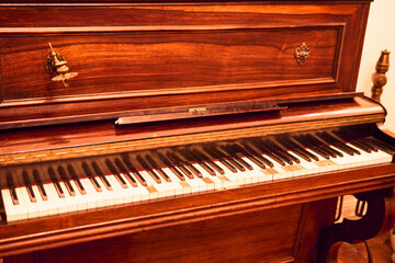 A classic wooden piano, seen in a wide view, colorful and in very good condition and preserved. Installed in a classic mansion, ready to play, with antique home decor.