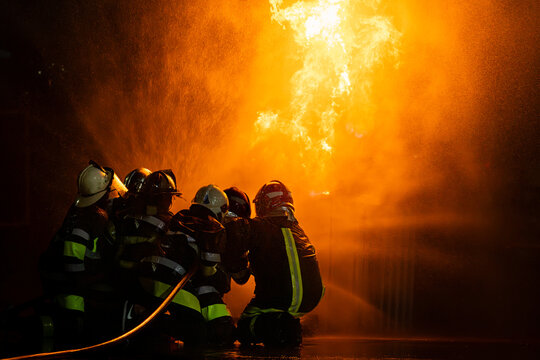 Silhouette of firefighters training for disaster relief officers.Firefighter using water and fire extinguishers to fight the flames in emergency situations in a dangerous area fire site on night time.