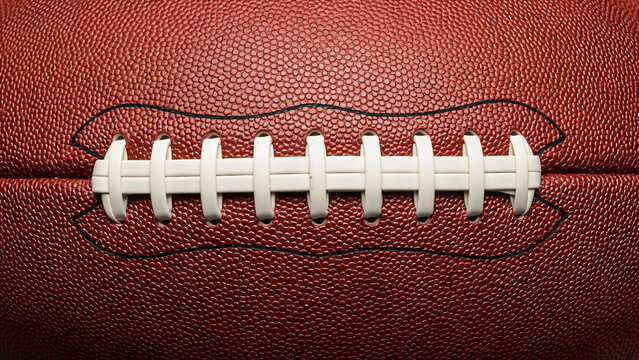 A close-up, high-fidelity photograph focuses intensely on the laces and textured leather surface of an American football ball.