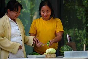Two women smiling while preparing cucumbers and cabbage for a meal.