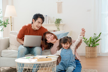 Asian family's happy work-life balance Father works remotely on a laptop while mother and daughter play together in a bright, modern living room.