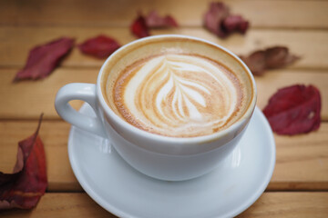 Coffee cup on wooden table with autumn leaves around