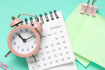 Calendar with alarm clock, sticky notes, paper clip and binder on turquoise background