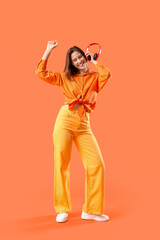 Happy young woman with modern headphones listening to music and dancing on orange background