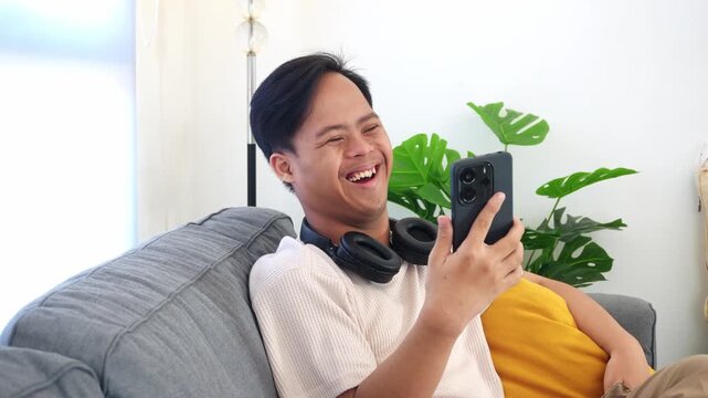 Joyful young asian man with asperger video chatting on phone while spreading smiles at home