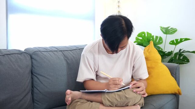 Creative boy with asperger sketching in notebook at home on comfortable couch relaxed