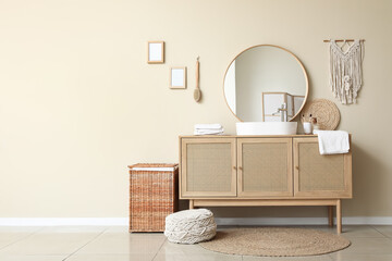 Chest of drawers and laundry basket near beige wall in stylish bathroom