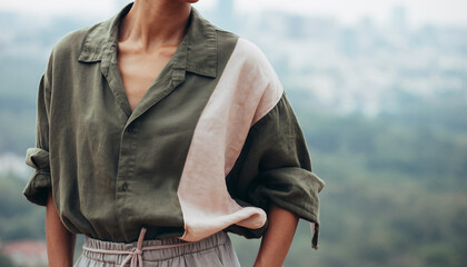 Woman wearing green shirt with rolled sleeves and scarf against blurred cityscape background with trees.