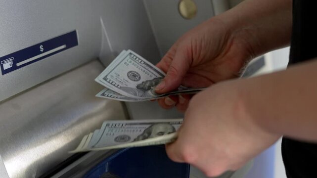 Hands holding several US hundred dollar bills in front of ATM. Person counting cash after withdrawal at bank machine as personal finance and money management concept