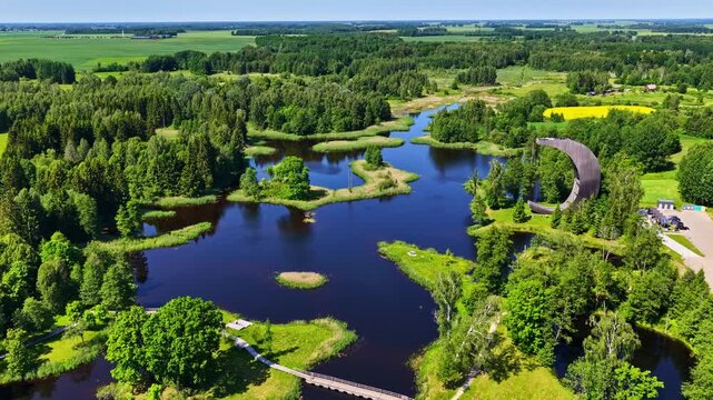 Aerial view of the Kirkilai Lakes and the curved observation tower in Biržai Regional Park, Lithuania. Scenic ponds, green forests, and winding walkways create a unique and peaceful natural landscape.