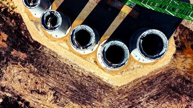 Aerial view of wind turbine foundations under construction, with large concrete tower bases and heavy machinery on the work site. A detailed look at renewable energy infrastructure.