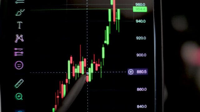 Pen tracking stock market candlestick chart on a dark digital display