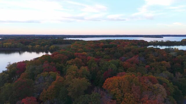 A calm Minnesota afternoon reveals a serene lake surrounded by a forest ablaze with vibrant autumn colors.