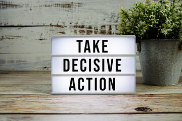 Take Decisive Action text on light box on wooden background