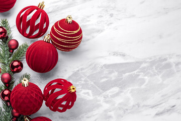 Red velvet baubles, Christmas ball ornaments and pine branches on marble table background, top view