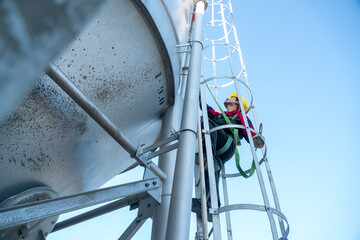 Low perspective shot of a maintenance worker climbing a steel ladder on a cylindrical tank, highlighting industrial engineering, risk awareness, and workplace safety.
