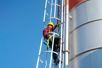 Engineer performing inspection work while climbing a steel ladder on an industrial tank, showing controlled movement and secure harness usage.