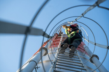 Worker viewed from below while climbing a tall industrial ladder cage, focusing on perspective, risk awareness, and professional safety procedures.
