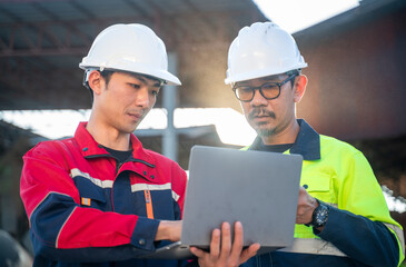 Engineers wearing safety helmets reviewing information on a laptop at industrial site, representing digital tools, collaboration, and site supervision.