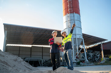 Engineers observing factory structure while holding laptop, representing site evaluation, safety awareness, and infrastructure assessment.