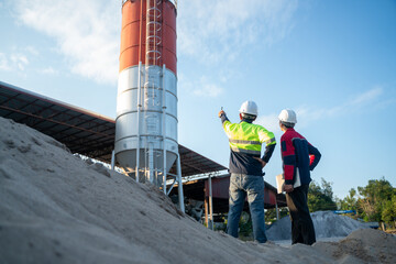 Wide-angle view of engineers standing on industrial ground facing a large silo, discussing site conditions and infrastructure planning under clear sky.