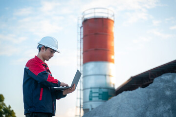 A data analyst monitoring factory performance metrics on a laptop while standing directly in front of the main production silo.