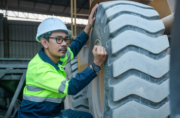 Professional industrial worker checking the tire tread and condition of heavy machinery during a routine maintenance inspection. He is wearing full PPE including a helmet and safety glasses