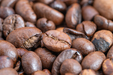 Macro view dark roast coffee pile with tight composition highlighting cracked surfaces and deep brown color, bold roasted aroma suggested by glossy oils and contrast