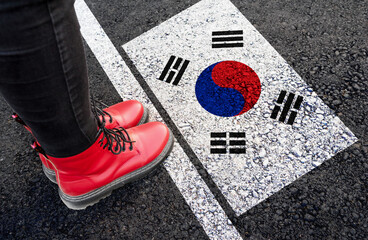 a woman with a boots standing on asphalt next to flag of South Korea and border
