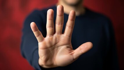 Hand with open palm and spread fingers in a stop gesture against a blurred red background