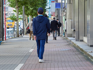 昼の東京都の繁華街で歩く中年男性と人々の姿